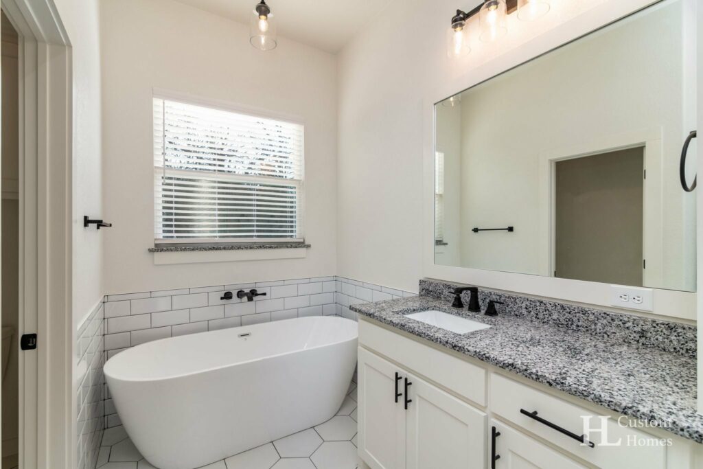Master bathroom with a white tub, granite countertop, and huge vanity mirror